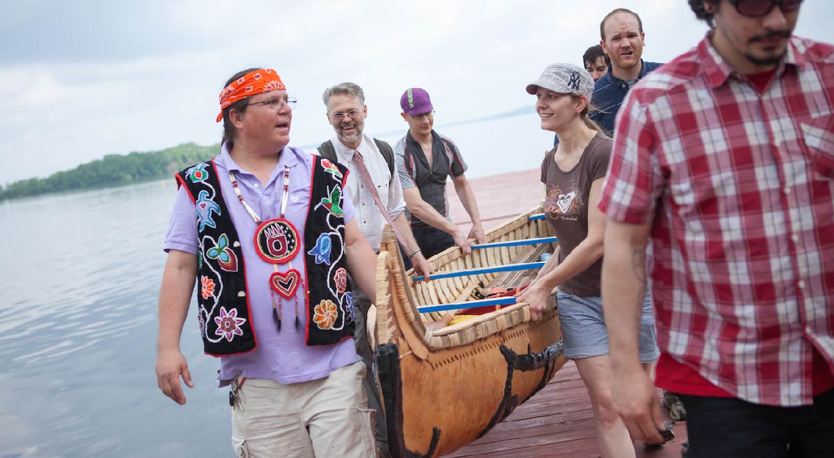 People carrying the Ojibwe birchbark canoe on a pier over Lake Mendota